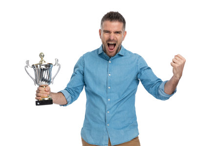 enthusiastic guy in denim shirt holding silver cup, celebrating victory, screaming and being happy...