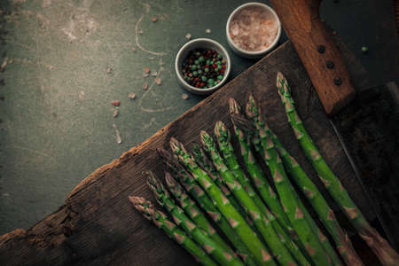 fresh sparrow grass on top of chopping board next to a cleaver and with two salt and pepper bowls in the backgroundの写真素材