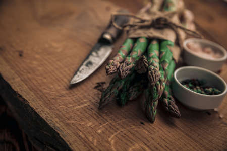 great cooking idea with fresh asparagus on top of old chopping board and salt, pepper and a knife next to itの写真素材