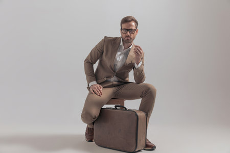 sexy businessman posing on a chair with his luggage between his legs and a cool attitudeの写真素材
