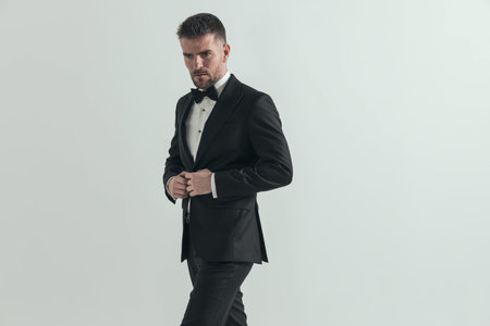 attractive businessman looking away with a tough attitude and arranging his tuxedo against gray...