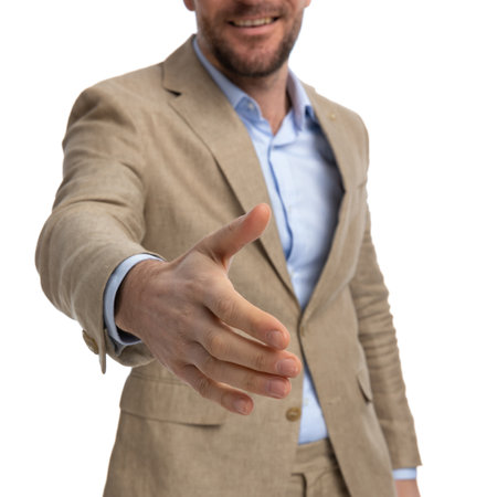 cutout picture of businessman in beige suit shaking hand, welcoming and smiling on white background in studioの写真素材