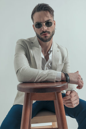 attractive businessman with open collar shirt holding arms on wooden chair and posing in a cool...