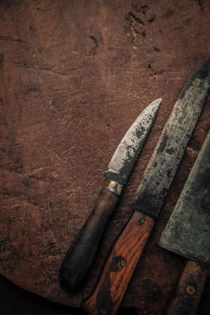 close up of small utility knives and kitchen knife with carbon steel blade on top of rustic old chopping boardの写真素材