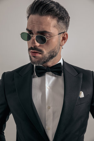 sexy businessman in tuxedo with sunglasses looking to side and posing on grey background in studioの写真素材