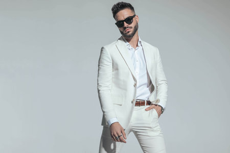 smart casual guy in white suit with open collar shirt holding hand in pocket and confidently posing on grey backgroundの写真素材