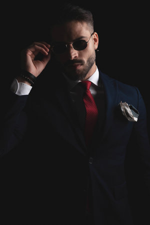 cut out picture of elegant guy in suit with red tie and handkerchief adjusting retro sunglasses in studioの写真素材