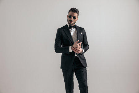 elegant businessman wearing black tuxedo and touching palms while posing in front of grey backgroundの写真素材