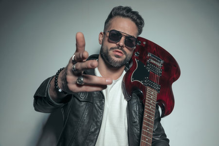 handsome rock singer with tough attitude holding one hand up and an electric guitar on his shoulderの写真素材