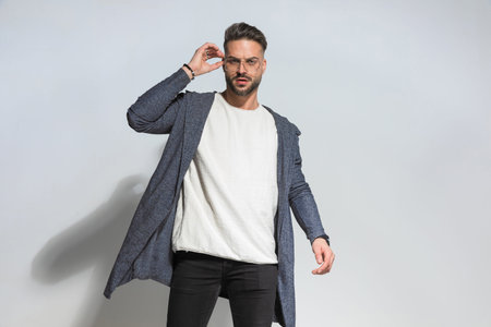 cool young guy wearing hoodie holding hand up and fixing eyeglasses while being confident and posing...
