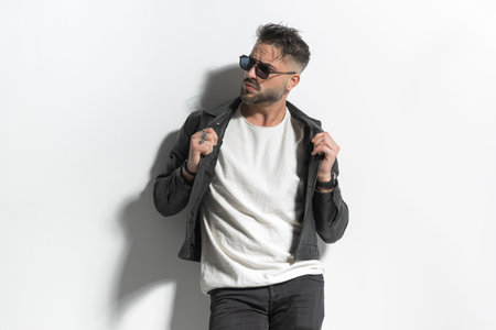 portrait of handsome cool guy with beard and wet hair pulling and adjusting jacket while looking to...