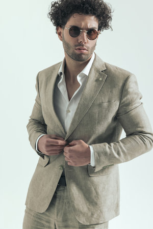 sexy turkish businessman being cool while adjusting and closing suit in front of grey background in studioの写真素材