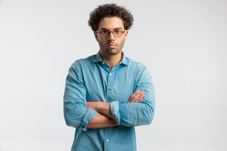 Portrait of young casual man crossing his arms at chest, standing, wearing a shirt and eyeglasses...