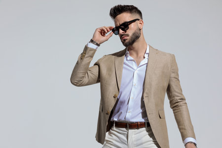 Portrait of attractive businessman arranging his sunglasses in a fashion pose, standing, against gray studio backgroundの写真素材