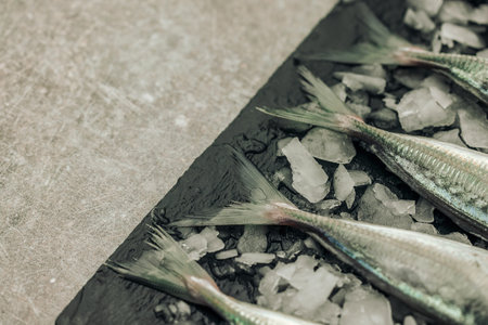 concept of freshness illustrated by uncooked white fish tails on chopping board with ice cubes on...
