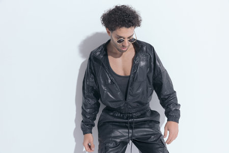 portrait of confident sexy man with leather suit and sunglasses looking down and posing while laying...