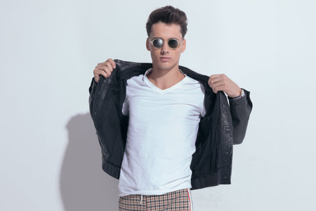 Portrait of  handsome casual man arranging his jacket on his body, standing, wearing sunglasses in a...