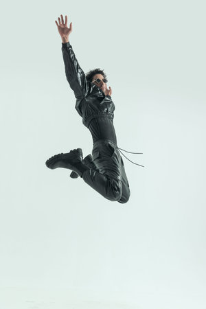 sexy casual man jumping and kicking with hands up, wearing a leather costume in a fashion poseの写真素材