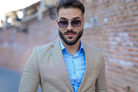 portrait of sexy bearded guy wearing sunglasses and posing outdoor in front of a bricks wall backgroundの写真素材
