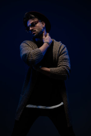 Portrait of attractive fashion model folding arms and touching neck, wearing a burgundy hat, eyeglasses and wool coat in dark studio backgroundの写真素材