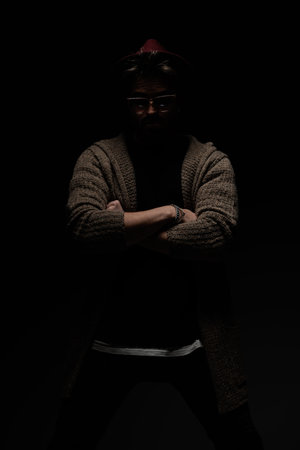 Portrait of young casual guy crossing his arms like a macho, wearing a burgundy hat, eyeglasses and...