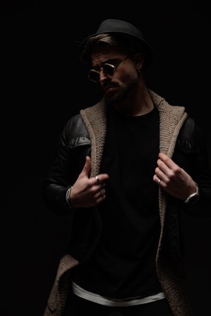 unshaved fahsion man looking to side and adjusting clothes while posing in a cool and confident manner on black backgroundの写真素材