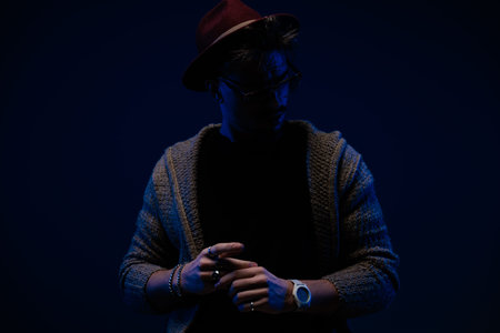 Portrait of attractive fashion man with mysterious vibe posing in dramatic stance, wearing a...