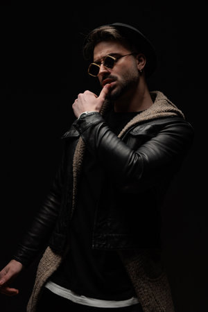 sexy young fashion man looking away while sensually touching lips in front of black backgroundの写真素材