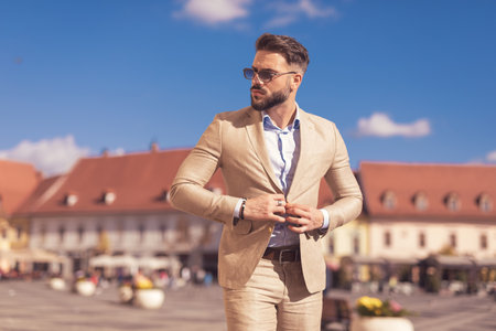 Portrait of young businessman opening his jacket and looking to the side, wearing sunglasses outdoor, in the old medieval townの写真素材