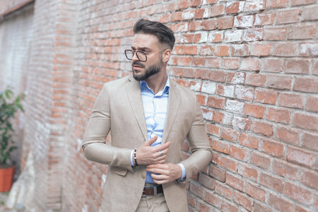Portrait of young businessman rubbing his palms and looking to side and wearing eyeglasses outdoor, in an old medieval townの写真素材