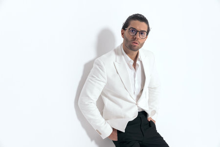 confident sexy man holding hands in pockets and laying on a wall in front of grey background in studioの写真素材