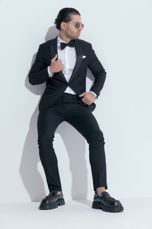 sexy businessman leaning on wall and arranging his tux, wearing glasses against white studio backgroundの写真素材