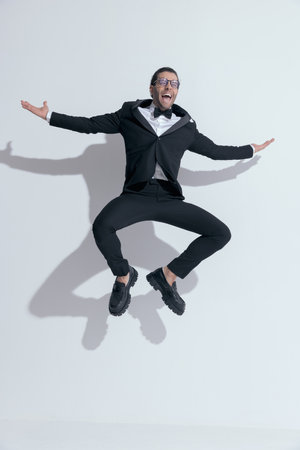 young businessman squatting in the air full of excitement, wearing glasses against white studio backgroundの写真素材