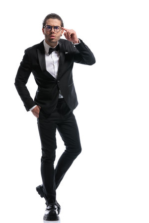 attractive businessman pointing at head with hand in pocket, legs crossed and wearing glasses against white studio backgroundの写真素材