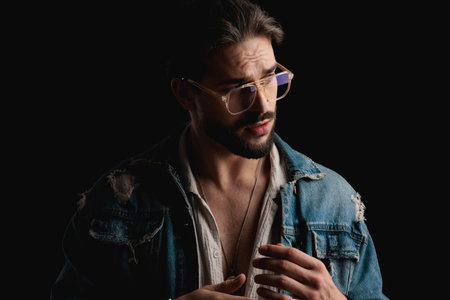 attractive casual man with glasses looking to side and posing in a fashion way in front of black background in studioの写真素材