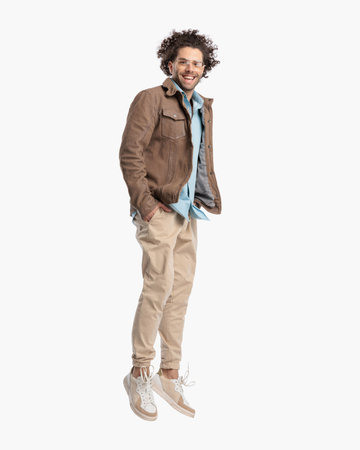 happy casual man with glasses jumping in the air with hands in pockets in front of white background in studioの写真素材