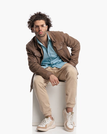 sexy confident man with curly hair holding hand in pocket and posing in front of white background in studioの写真素材
