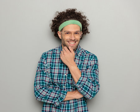 excited casual man with headband and glasses folding arms and laughing while standing on grey backgroundの写真素材