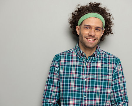 portrait of happy casual guy with glasses and headband smiling and posing while wearing sport headband on grey backgroundの写真素材