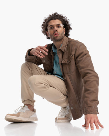 sexy casual guy with glasses crouching and posing in a cool way in front of white background in studioの写真素材
