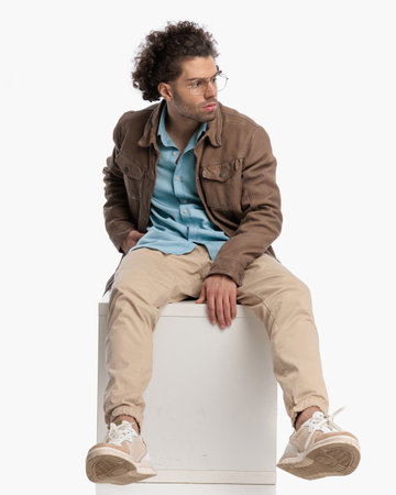 fashion young model with curly hair looking to side and posing with hand in pocket in front of white backgroundの写真素材