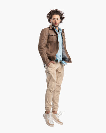 side view of casual man with curly hair leaping up with hands in pockets in front of white backgroundの写真素材