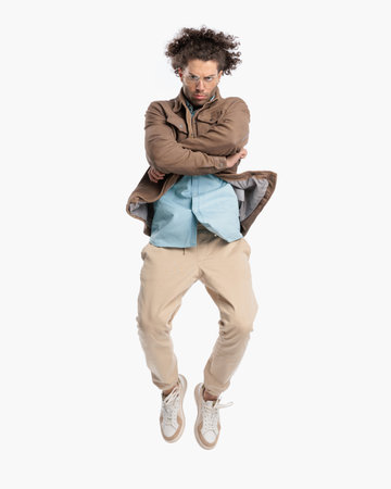 upset casual man with glasses and curly hair jumping in the air, frowning and crossing arms in front of white background in studioの写真素材
