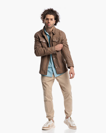 full body picture of handsome man with curly hair and glasses adjusting jacket and walking in front of white background in studioの写真素材