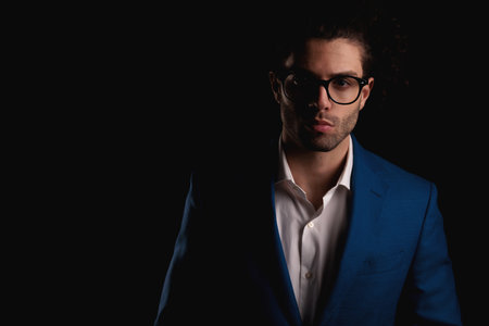 sexy businessman with glasses wearing suit with open collar shirt while looking forward in front of black background in studioの写真素材