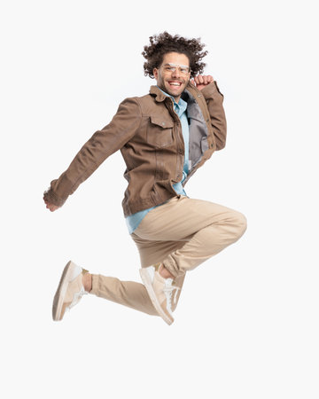 side view of dynamic casual man laughing and leaping up in the air in front of white background in studioの写真素材