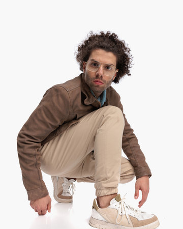 side view of confident cool man with curly hair crouching and looking forward in front of white background in studioの写真素材