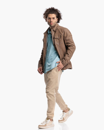 side view of sexy man with curly hair walking with hand in pocket in front of white background in studioの写真素材