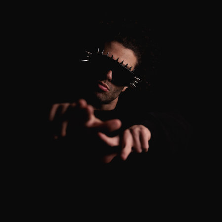 sexy mysterious man with cool sunglasses making hand gesture and pointing fingers forward in front of black backgroundの写真素材