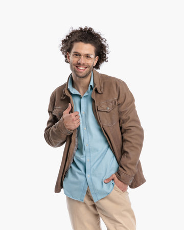 happy cool man with glasses holding hands in pockets and laughing  while adjusting jacket and posing in front of white background in studioの写真素材